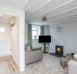 A living room with a TV on a stand a fireplace two armchairs and a small ottoman at Oscars Pad in Brynsiencyn