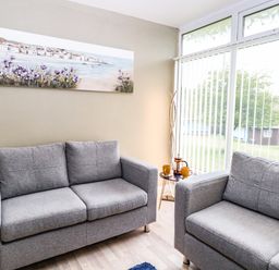 A sitting area with two grey sofas and a small round table with cups and a teapot by a window at Chalet 126a in Cromer