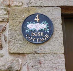 A round sign with the number 4 and text Rose Cottage mounted on a stone wall at Rose Cottage Akeld near Wooler