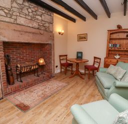 A sitting room with a stone fireplace wooden furniture and green upholstered seating at Rose Cottage Akeld near Wooler