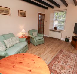 A living room with green sofa and armchair wooden table lamp and television at Rose Cottage Akeld near Wooler