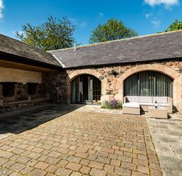 An outdoor seating area with stone walls and paved surface at Lupin Cottage near Wooler