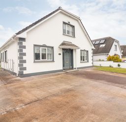 A white house with gray trim a concrete driveway and a small lawn at 17 Clover Hill in Killorglin County Kerry