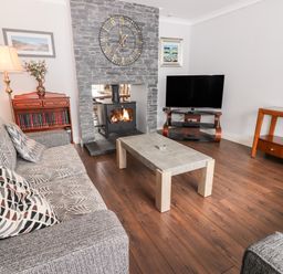 A living room with a sofa a coffee table a TV on a stand a stone fireplace with a clock and a wooden cabinet with books at 17 Clover Hill in Killorglin County Kerry