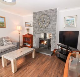 A living room with a stone fireplace and clock a television on a stand a sofa and a coffee table at 17 Clover Hill in Killorglin County Kerry