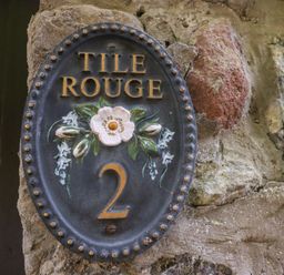 A decorative house number plaque with the text Tile Rouge 2 on a stone wall at Tile Rouge in Wooler