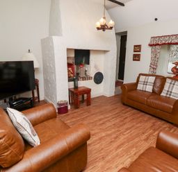 A living room with brown leather sofas a television and a fireplace at Tile Rouge in Wooler