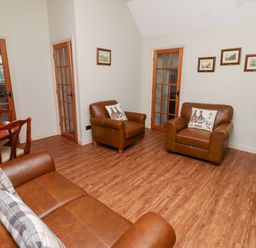 A living room with leather armchairs sofa wooden dining table and television at Tile Rouge in Wooler