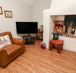 A room with a brown leather armchair a television on a stand framed paintings on the wall and a nook with decorative items at Tile Rouge in Wooler