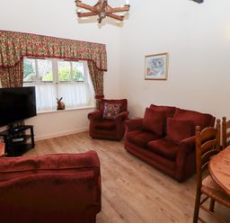 A living room with red sofas a wooden dining table chairs a television on a stand and a window with floral curtains at Pansy Plot in Akeld near Wooler