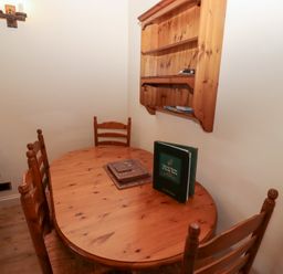 A dining area with a wooden table and four chairs next to a wall-mounted wooden shelf and a brown sofa at Pansy Plot in Akeld near Wooler