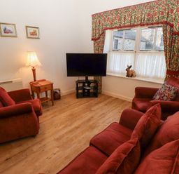 A living room with red sofas a wooden side table a floor lamp a television and floral curtains at Pansy Plot Akeld near Wooler