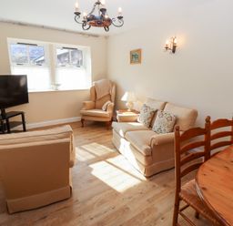 A living room with sofas a wooden dining table and chairs a television and a window at Catkin Cottage in Akeld near Wooler