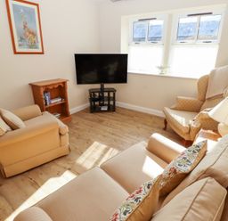 A living room with beige sofas armchair wooden floor TV and bookshelf at Catkin Cottage Akeld near Wooler