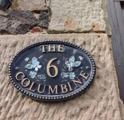 A house number plaque showing the number 6 and the name The Columbine on a stone wall at The Columbine in Akeld near Wooler