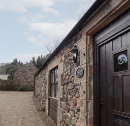 Stone buildings with a cobblestone path between them and a dark wooden door at The Columbine in Akeld near Wooler