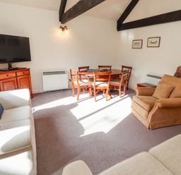 A living room with two beige sofas a brown armchair a wooden dining table with six chairs a wooden cabinet with a television and exposed ceiling beams at The Columbine in Akeld near Wooler