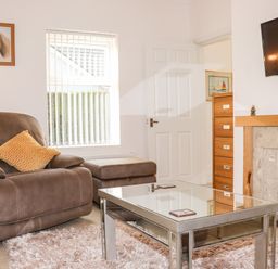 A living room with a brown armchair and footstool a glass coffee table a fireplace with mantel and TV mounted above at Lane Cottage in Ballycullane County Wexford