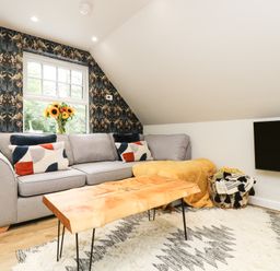 A living room with a gray sofa cushions and a wooden table with a rug on the floor and a wall-mounted TV at Robin's Nest at The Shire Inn in Killivose near Camborne