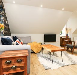 A living room with a gray sofa a wooden coffee table a wooden side table a dark gray armchair and a wall-mounted TV at Robins Nest at The Shire Inn in Killivose near Camborne