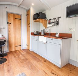 A kitchen with wooden floor blue cabinets a TV on the wall and a small dining area at The Moorhen Retreat in Nantmawr near Trefonen