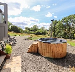 An outdoor area with a wooden hot tub gravel ground and garden chairs at The Moorhen Retreat in Nantmawr near Trefonen