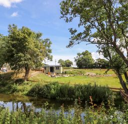A small building with chairs outside near trees and a pond at The Moorhen Retreat in Nantmawr near Trefonen