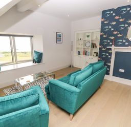 A living room with teal sofas a glass coffee table and patterned wallpaper at 21 The Rest in Porthcawl