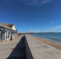 A seaside walkway with a fish and chips shop on the left and a beach with water on the right at Wrens Nest in Slapton