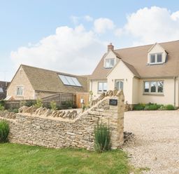 A stone wall in front of a two story house with a gravel driveway at Tawny Cottage Fulbrook near Burford