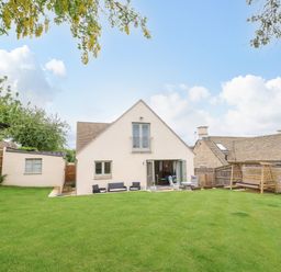A backyard with green grass and outdoor seating in front of a cream house with a balcony at Tawny Cottage in Fulbrook near Burford