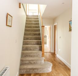 A carpeted staircase with wooden handrail in a hallway with wooden floor and open doors at Tawny Cottage in Fulbrook near Burford