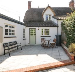 An outdoor patio area with a black bench two wooden chairs and a table beside a white building with a thatched roof at 1 Old Thatch in Kilve