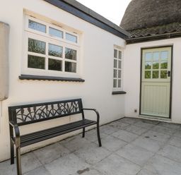 An outdoor patio with a metal bench next to a green door and two windows at 1 Old Thatch in Kilve