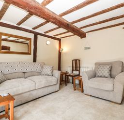 A living room with beige sofa and armchair wooden beams on ceiling and walls at 1 Old Thatch Kilve