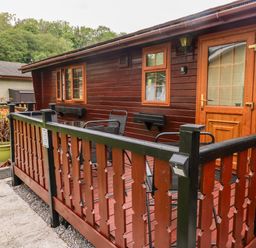 A wooden cabin with a porch featuring outdoor chairs and a table surrounded by a wooden railing at Heritage Park in Stepaside near Kilgetty