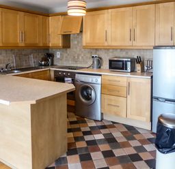 A kitchen with wooden cabinets a washing machine a microwave and a refrigerator at Apartment One in Duncannon County Wexford