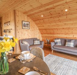 A living room with wooden walls two grey sofas a dining table set with plates and yellow flowers at Bluebell St Harmon near Rhayader