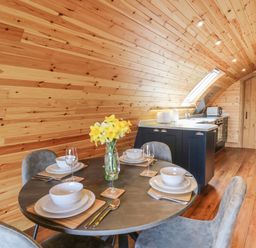 A dining area with a round table set for four and a kitchen with wooden walls and ceiling at Bluebell in St Harmon near Rhayader