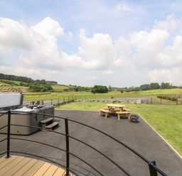 An outdoor space with a hot tub bench picnic table and fire pit overlooking a grassy field and trees at Bluebell in St Harmon near Rhayader