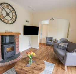 A living room with a wood burning stove a wall clock a sofa and two armchairs at Ger Yr Afon Cottage in St Harmon near Rhayader