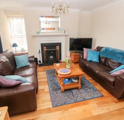 A living room with two brown leather sofas a wooden coffee table with flowers a fireplace and a television at The Old Bakery in Milton Tenby