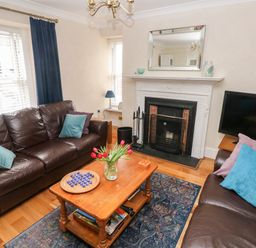 A living room with brown leather sofas a wooden coffee table with flowers a fireplace and a television at The Old Bakery in Milton Tenby