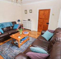 A living room with brown leather sofas and a wooden coffee table with flowers at The Old Bakery in Milton Tenby