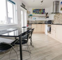 A kitchen with light wood cabinets a black dining table with black chairs and colorful wall art at Fistral Drift in Newquay
