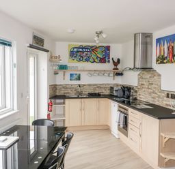 A kitchen with wooden cabinets black countertops dining table with chairs and colorful wall art at Fistral Drift in Newquay