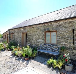 An exterior stone wall with windows and a door surrounded by various potted plants and a metal bench at Golwg Las in Pumsaint near Lampeter