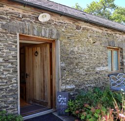 Stone exterior wall with an open wooden door a window a metal bench and plants at Golwg Las Pumsaint near Lampeter