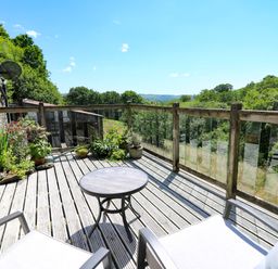 An outdoor deck with two chairs a round table potted plants and a wooden railing overlooking trees and hills at Golwg Las in Pumsaint near Lampeter