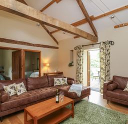 A living room with brown leather sofas a wooden coffee table and an open door leading outside at Nant Glas in Pumpsaint near Lampeter